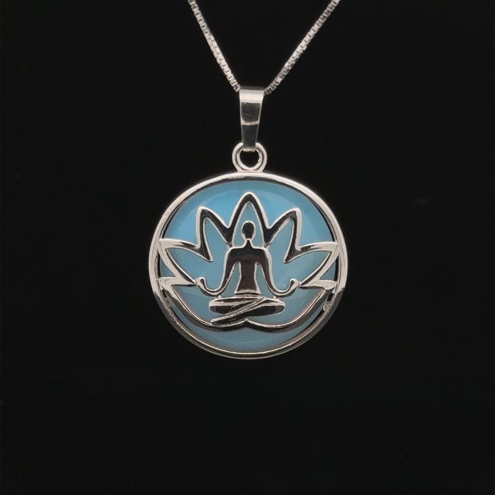 
                  
                    A Silver Plated Lotus Meditation Pendant with Gemstone features a lotus design with a seated meditation figure at its center, set against a light blue background. The pendant hangs on a thin silver chain. Black background.
                  
                