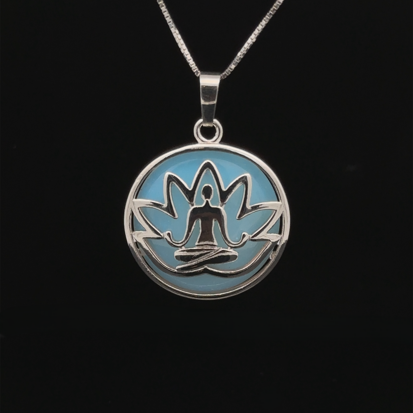 
                  
                    A Silver Plated Lotus Meditation Pendant with Gemstone features a lotus design with a seated meditation figure at its center, set against a light blue background. The pendant hangs on a thin silver chain. Black background.
                  
                
