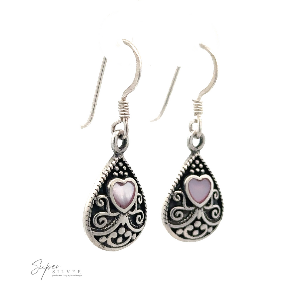 
                  
                    A pair of Bali Style Teardrop Earrings with Inlaid Stone, with intricate filigree designs and pink mother-of-pearl heart-shaped accents, crafted from sterling silver and hanging on simple ear hooks.
                  
                
