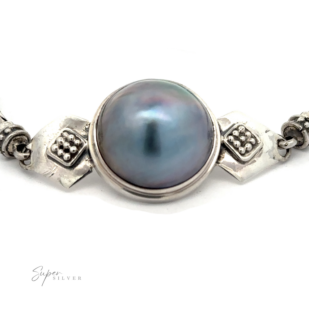 Close-up of a silver necklace featuring a round, grayish-blue pearl set in an ornate silver setting. The brand name "Blue Mabe Pearl Bali Bracelet" is visible in the bottom left corner, reminiscent of the intricate style found in Bali crafted jewelry.