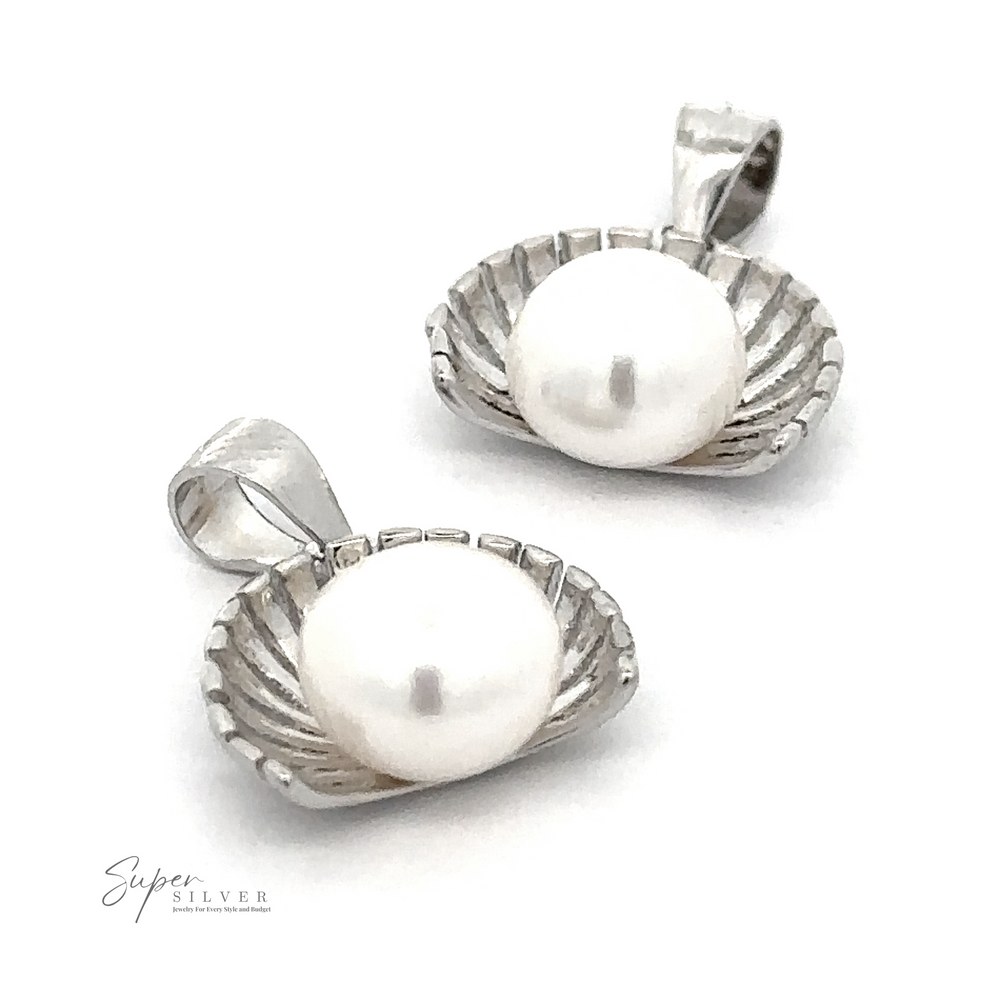 Two Pearl Pendant with Shell Background charms shaped like petite half shells, each holding a fresh water pearl, are displayed against a white background. The logo 