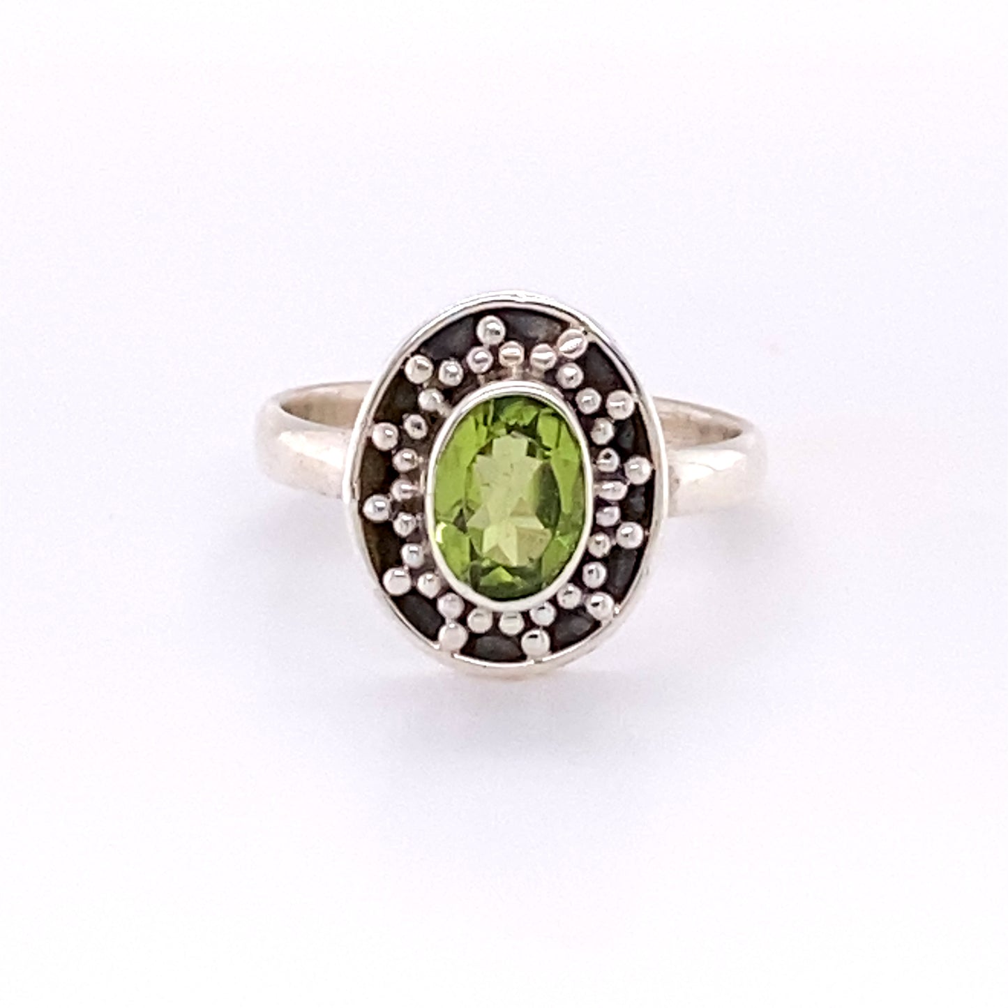 The Oval Peridot Dotted Shield Ring featuring an oval green gemstone surrounded by decorative Bali-styled disk setting and intricate silver beadwork.