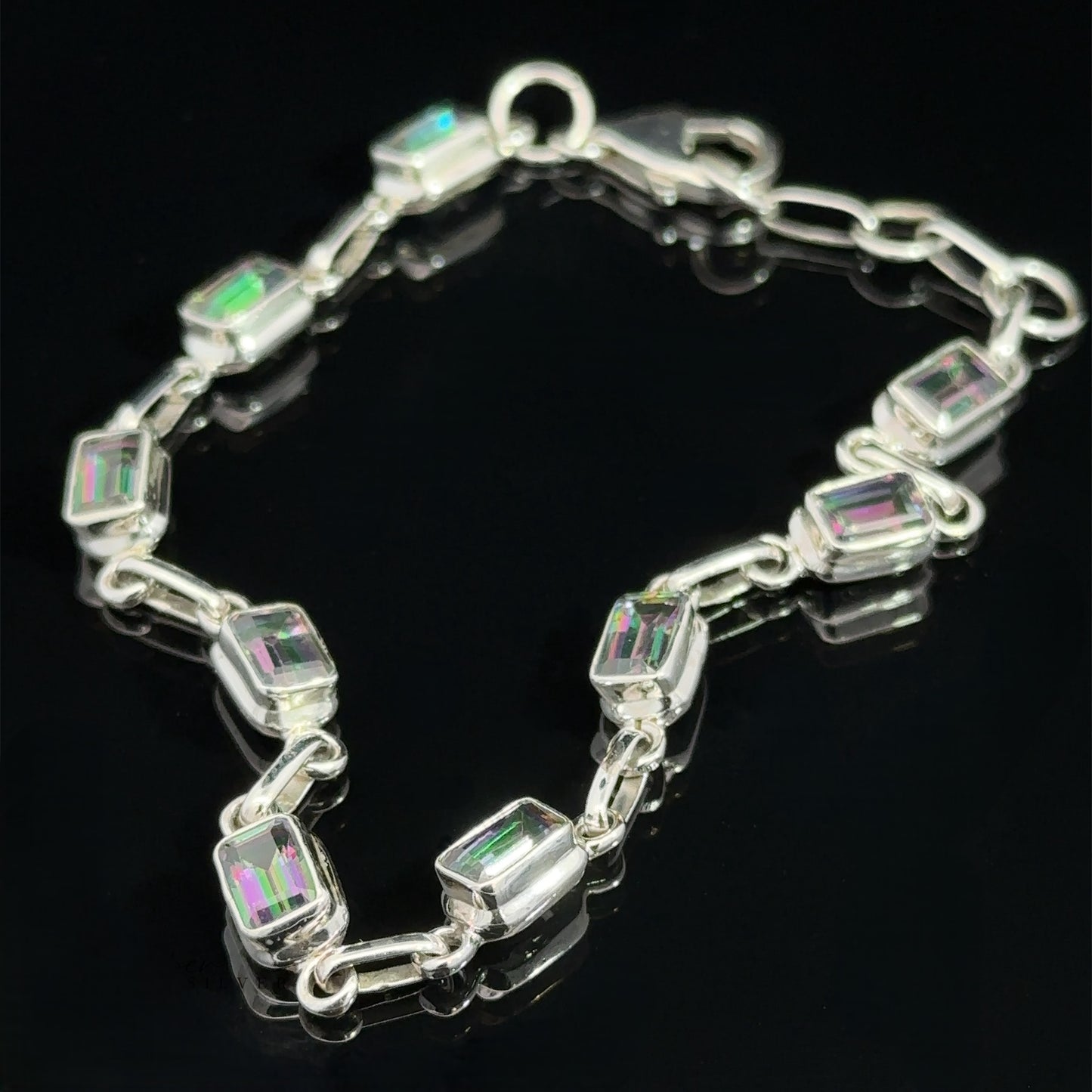 
                  
                    Rainbow Mystic Topaz Rectangle Link Bracelet featuring rectangular iridescent gemstones linked together, displayed on a black surface.
                  
                