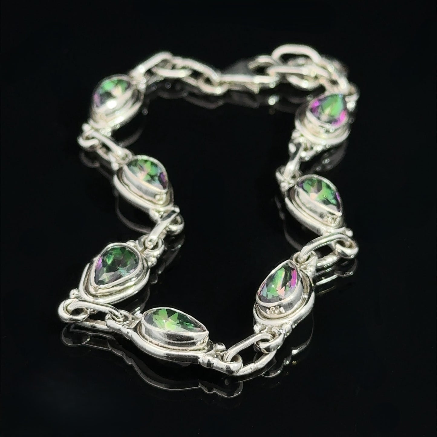 
                  
                    A Rainbow Topaz Bordered Teardrop Bracelet with nine teardrop-shaped, green and purple gemstones linked together, displayed on a black background.
                  
                