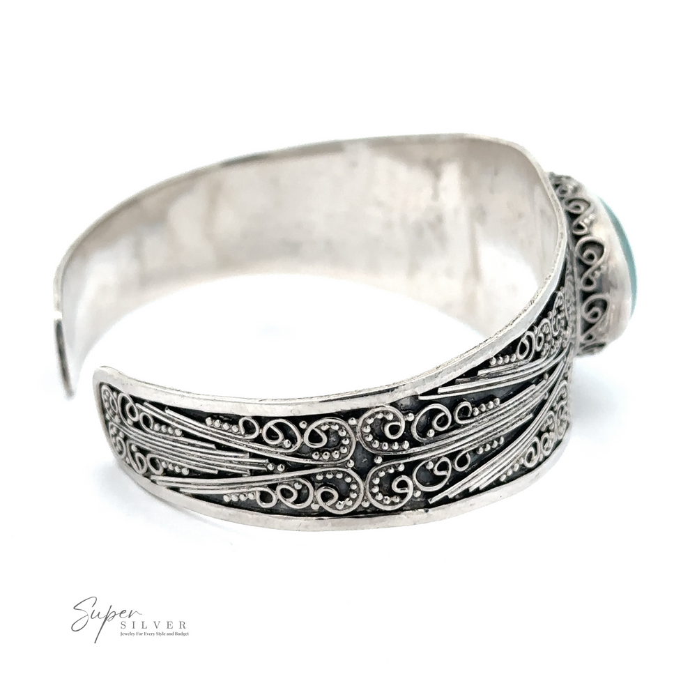 An intricately designed .925 Sterling Silver cuff bracelet with ornate patterns and a prominent round genuine turquoise stone. Engraved with the "Genuine Turquoise Bali Cuff Bracelet" logo.