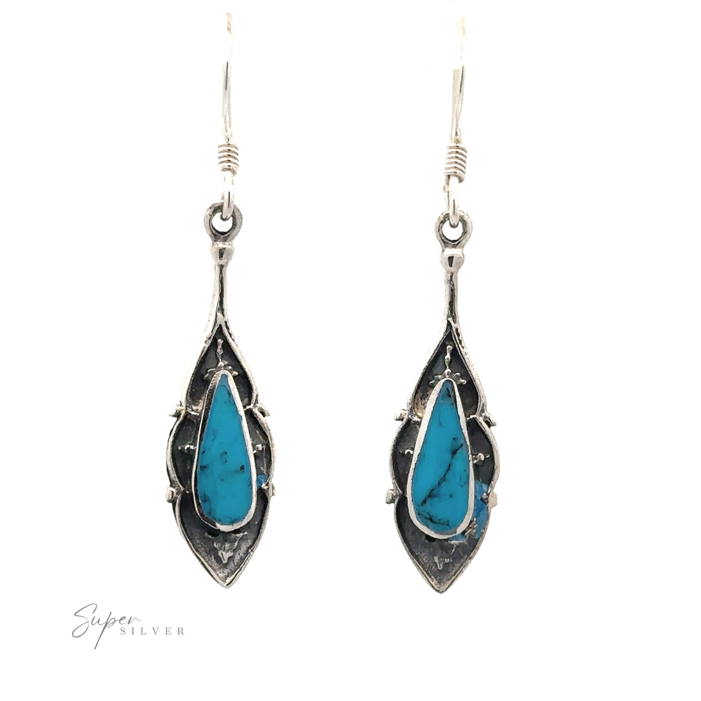 
                  
                    A pair of Teardrop Shape Inlaid Earrings with turquoise stones set in an ornate, oxidized finish design, hanging from hooks on a white background.
                  
                