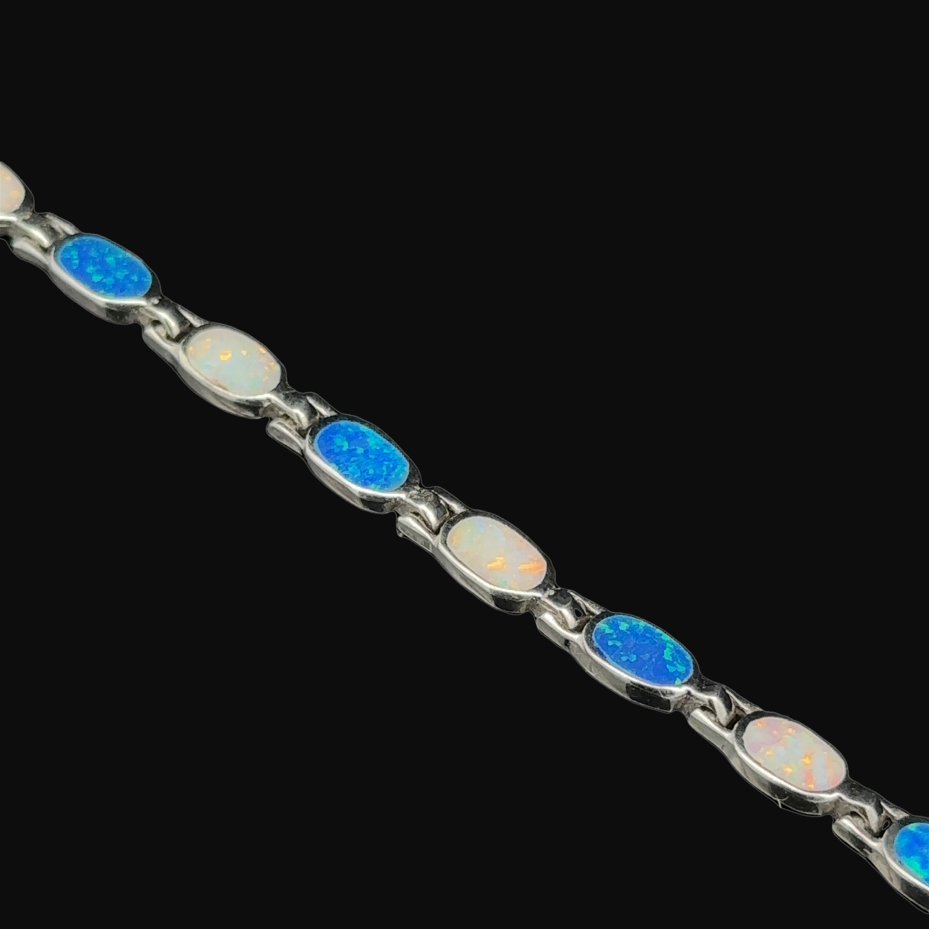 The Oval Lab-Created Opal Bracelet features alternating opal and blue stone oval settings set against a black backdrop, all meticulously crafted in .925 sterling silver, adding a touch of modern elegance.