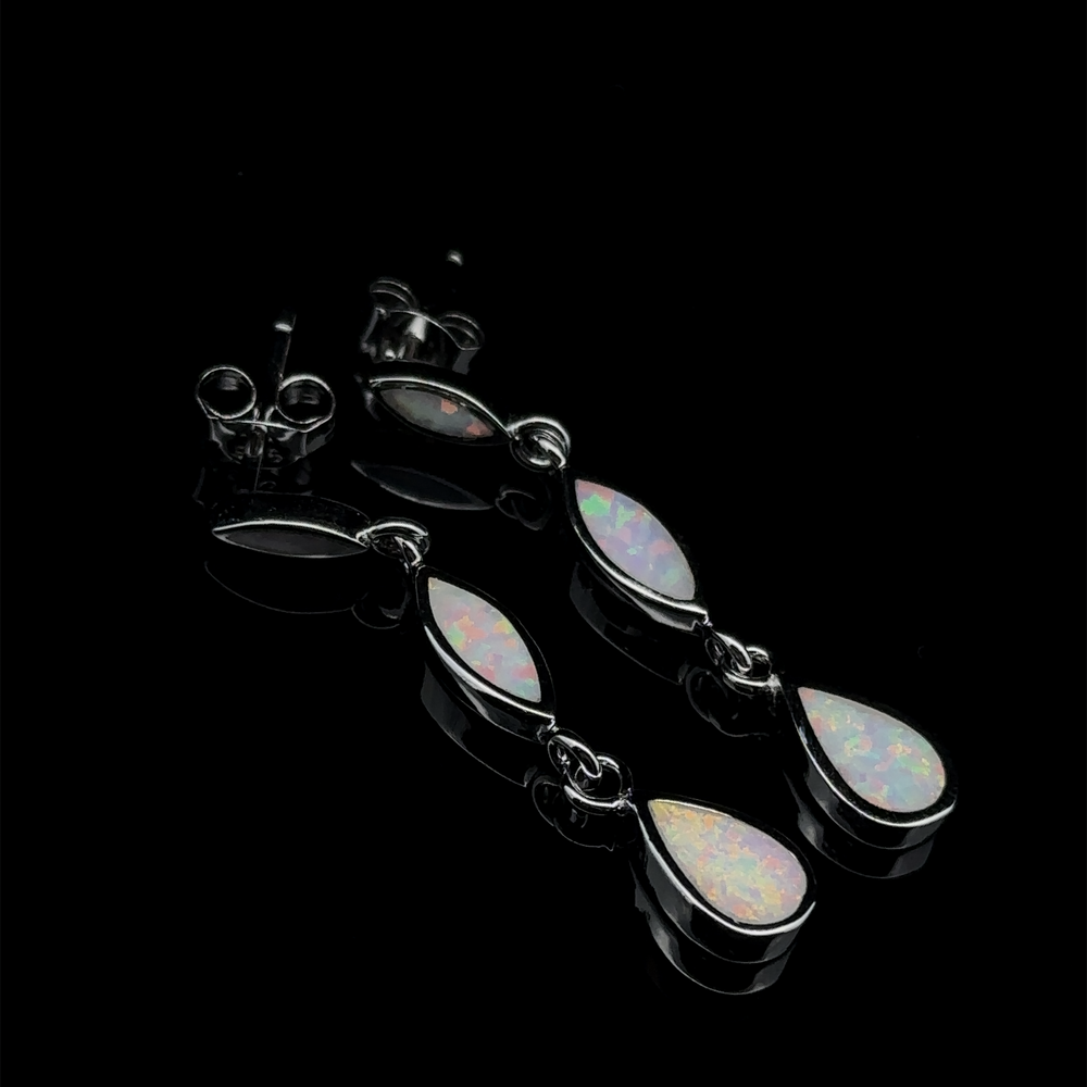 
                  
                    A pair of Elegant Lab-Created Opal Earrings with oval and teardrop-shaped stones, placed on a glossy black surface.
                  
                