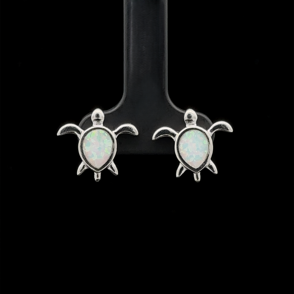 
                  
                    The Simple Lab-Created Opal Turtle Studs, a pair of small sterling silver sea turtle stud earrings featuring lab-created opal stones, are displayed against a black background.
                  
                