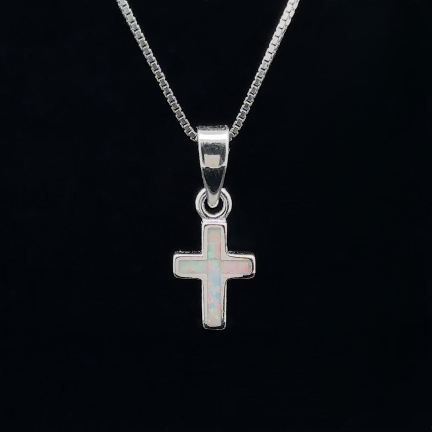 
                  
                    A Lab-Created Opal Cross Pendant, crafted from .925 Sterling Silver, glistens elegantly on a chain against a black background.
                  
                