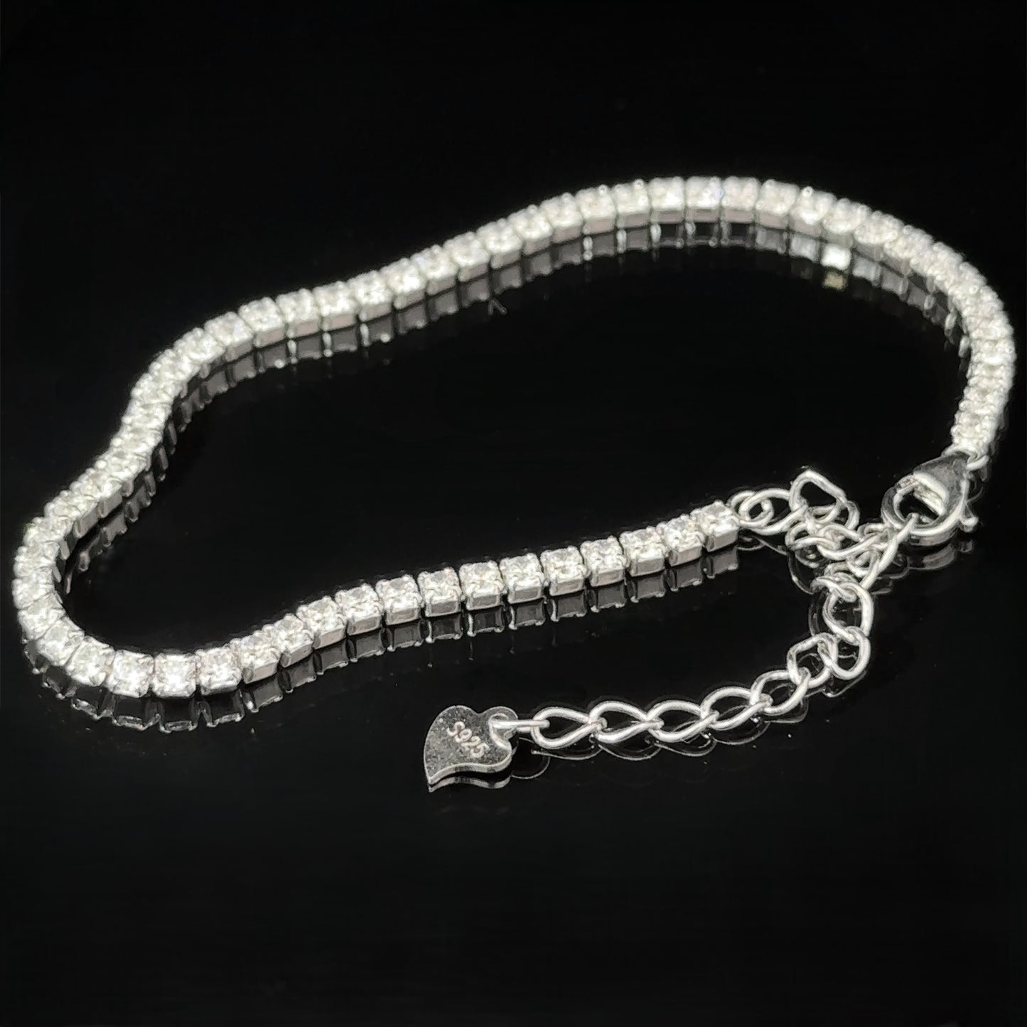 
                  
                    A Square Cubic Zirconia Tennis Bracelet featuring a row of square-cut cubic zirconia crystals and a heart-shaped charm on the rhodium-plated sterling silver chain, displayed against a black background.
                  
                