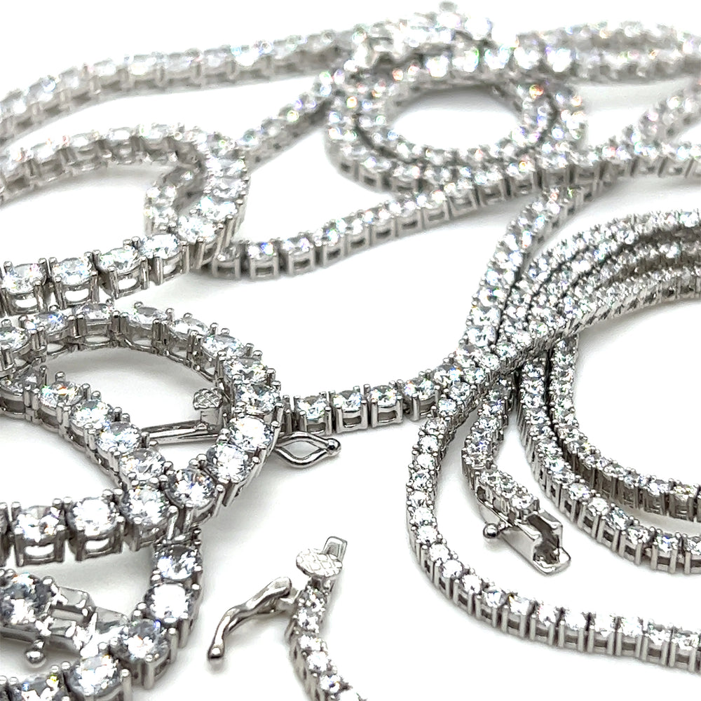 A stunning collection of Super Silver cubic zirconia tennis necklaces and bracelets adorned with glistening cubic zirconia, elegantly displayed on a sleek white surface.