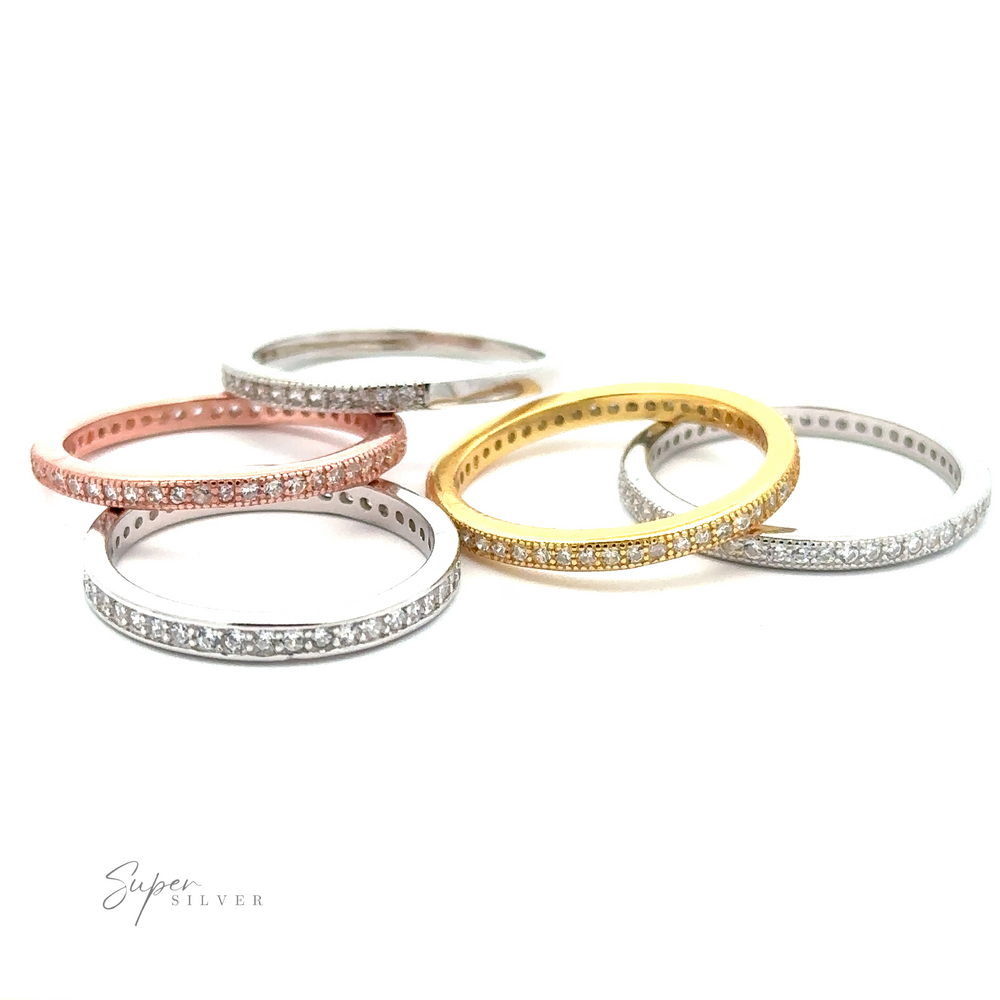 Five Classic Pave Cubic Zirconia Eternity Rings with different colored plating (rose gold, silver, and gold) and small embedded cubic zirconia crystals are displayed in a row on a white background.