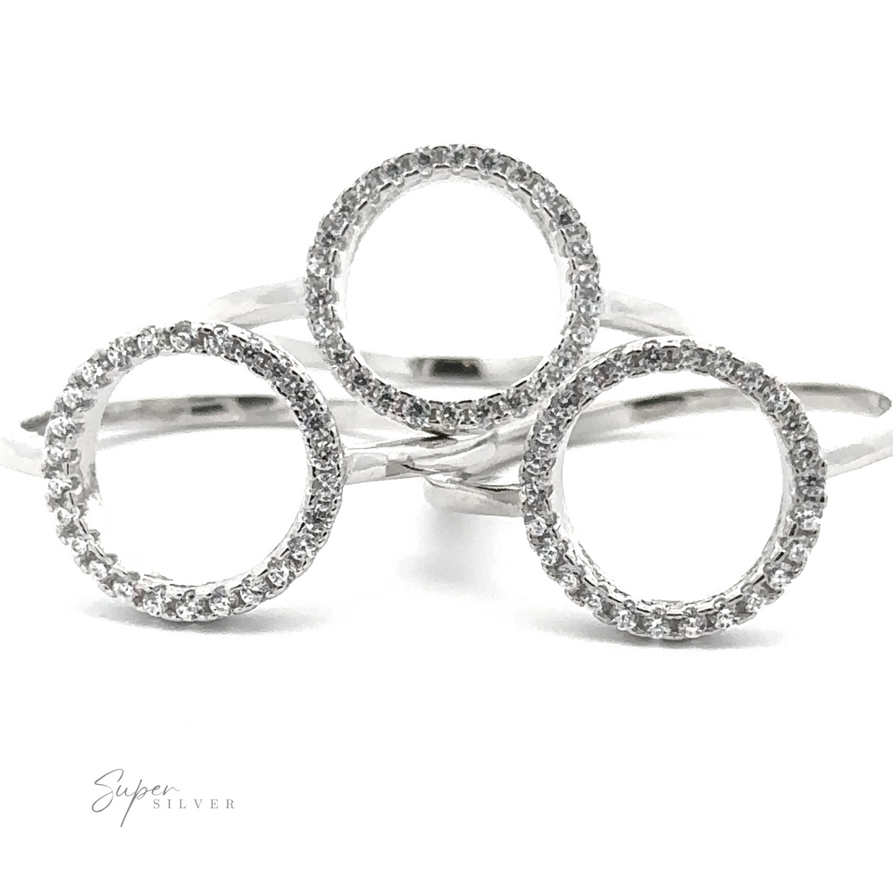 
                  
                    Three Modern Circular Pave Cubic Zirconia Rings, arranged in a triangular formation, exude contemporary elegance. Each ring dazzles with its gem-encrusted design, offering brilliant sparkle. The "Super Silver" logo adorns the bottom left corner.
                  
                