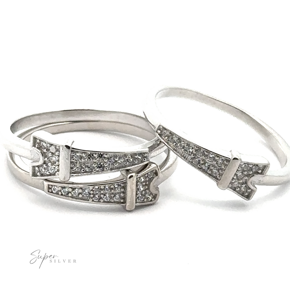 
                  
                    The Pave Cubic Zirconia Eiffel Tower Ring, featuring two silver bands with buckle designs and shimmering stones, exudes Parisian elegance against a white background.
                  
                