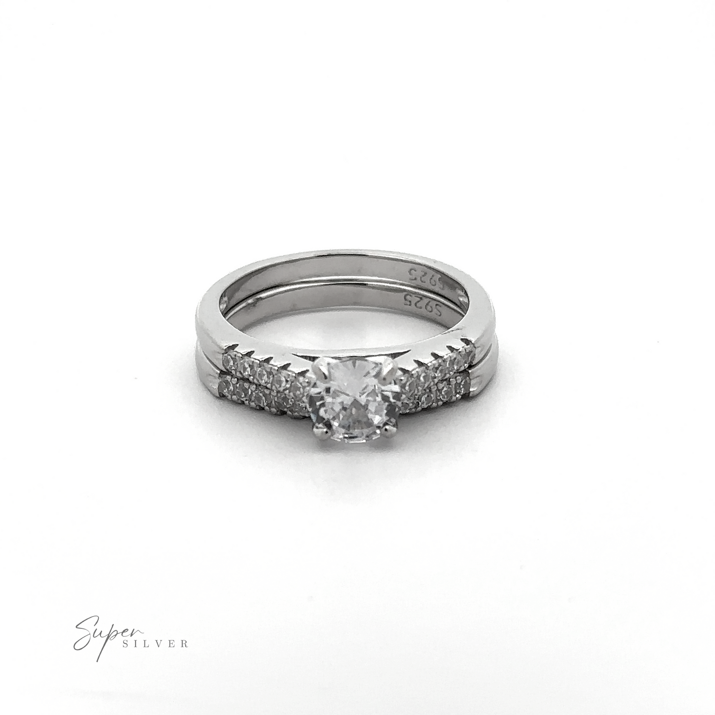 
                  
                    The Round Solitaire Wedding Band Set features a central diamond with small diamonds adorning the sterling silver band, all displayed atop a plain white background. The rhodium finish adds an extra touch of elegance to this timeless piece.
                  
                