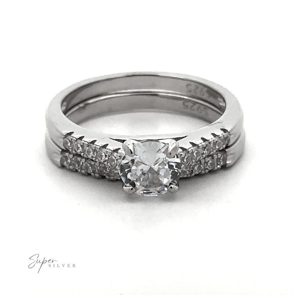 
                  
                    Introducing the Round Solitaire Wedding Band Set: a stunning sterling silver engagement ring with a central diamond, accentuated by small diamonds on the band. The set is complemented by a matching wedding band featuring cubic zirconia. Both rings are inscribed with "925," highlighting their exquisite quality rhodium finish.
                  
                