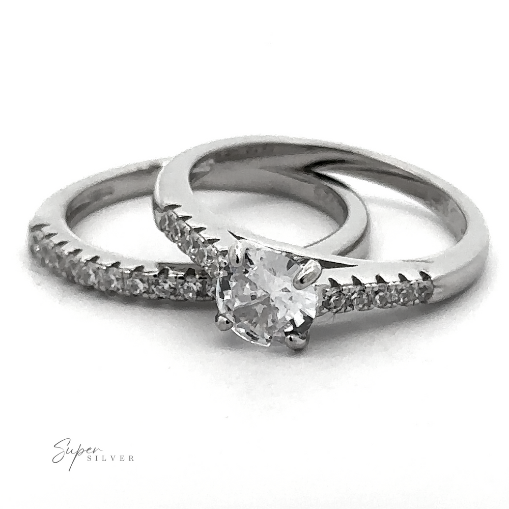 Two stunning sterling silver rings from the "Round Solitaire Wedding Band Set" are displayed; one is a plain band adorned with small diamonds, and the other showcases a larger central diamond. The elegant design is accentuated by a rhodium finish, adding an extra touch of sophistication. The brand "Super Silver" is visible in the bottom left corner.