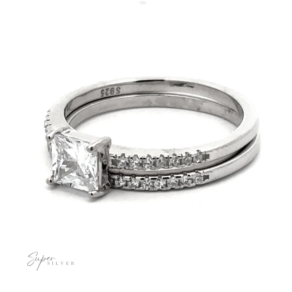 
                  
                    Princess Cut Cubic Zirconia Wedding Band Set featuring a princess cut cubic zirconia central stone and a band with smaller inset stones, all enhanced by a rhodium finish.

                  
                