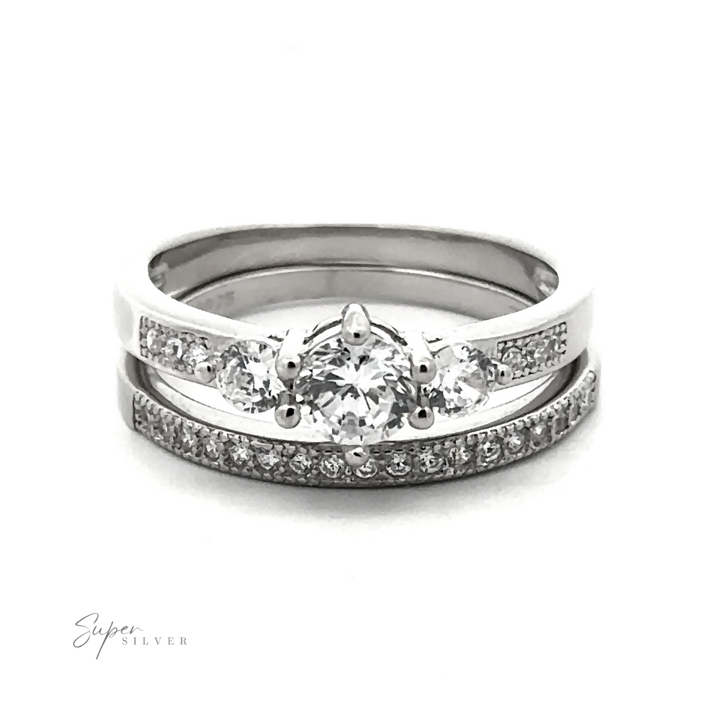 
                  
                    A Round Cubic Zirconia Wedding Band Set; the upper ring features three larger diamonds, and the lower ring is adorned with smaller high-quality cubic zirconia stones in a continuous line. This affordable wedding set offers elegance without compromise.
                  
                
