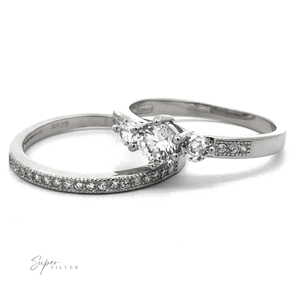 A pair of silver rings; one features a central trio of high-quality cubic zirconia stones with smaller stones on the band, and the other is an eternity ring with embedded diamonds. This affordable Round Cubic Zirconia Wedding Band Set radiates elegance without compromising on quality.