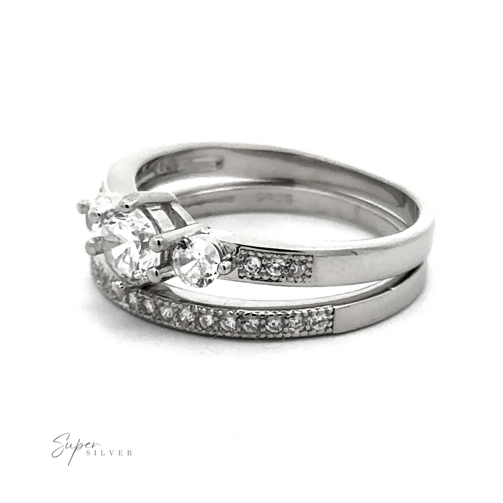 
                  
                    A set of two silver rings, one featuring three large round-cut high-quality cubic zirconia stones and the other adorned with smaller gemstones along the band. This Round Cubic Zirconia Wedding Band Set is displayed on a white background.
                  
                