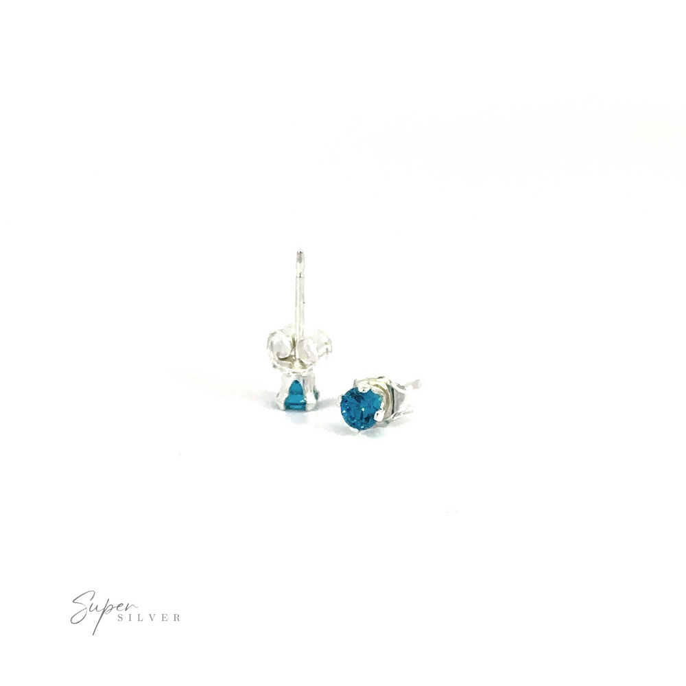 
                  
                    A pair of blue Round CZ stud earrings on a white background with a signature at the bottom.
                  
                