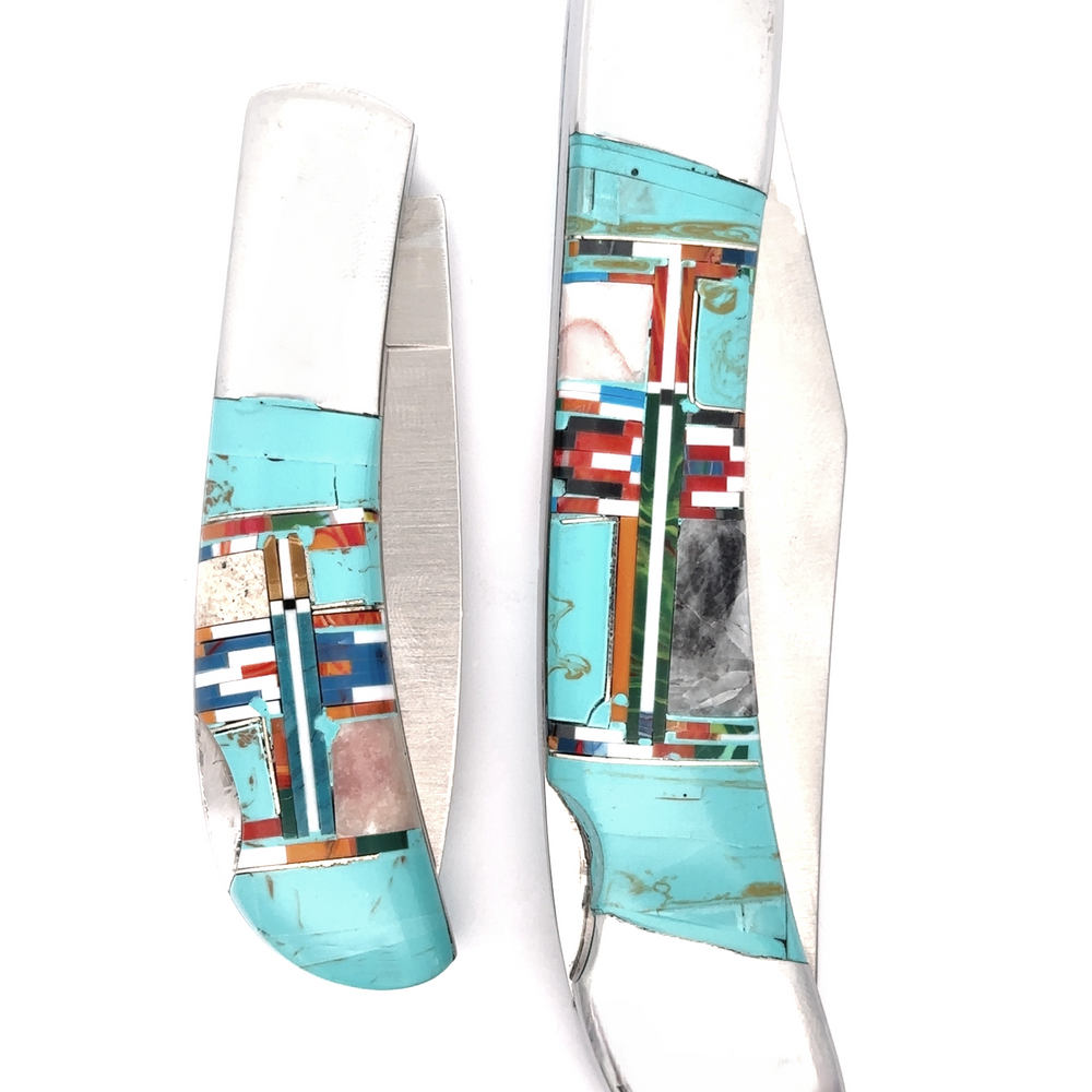 
                  
                    Two Intricate Inlay Southwest Pocket knives display detailed turquoise, red, blue, and white inlaid designs on their handles, capturing a unique Southwest style against a white background. One knife is open while the other remains closed.
                  
                