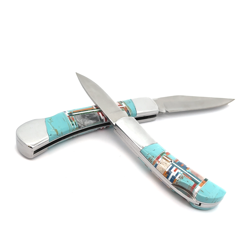 
                  
                    The "Intricate Inlay Southwest Pocket Knife," featuring turquoise and mosaic-patterned handles, showcases two blades open and crossed on a white background, embodying an elegant Southwest aesthetic.
                  
                