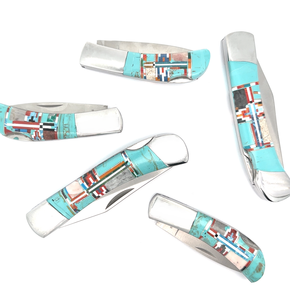 A selection of five Southwest-style pocket knives, each featuring intricate turquoise and red inlay designs on the handles, are arranged randomly on a white background.