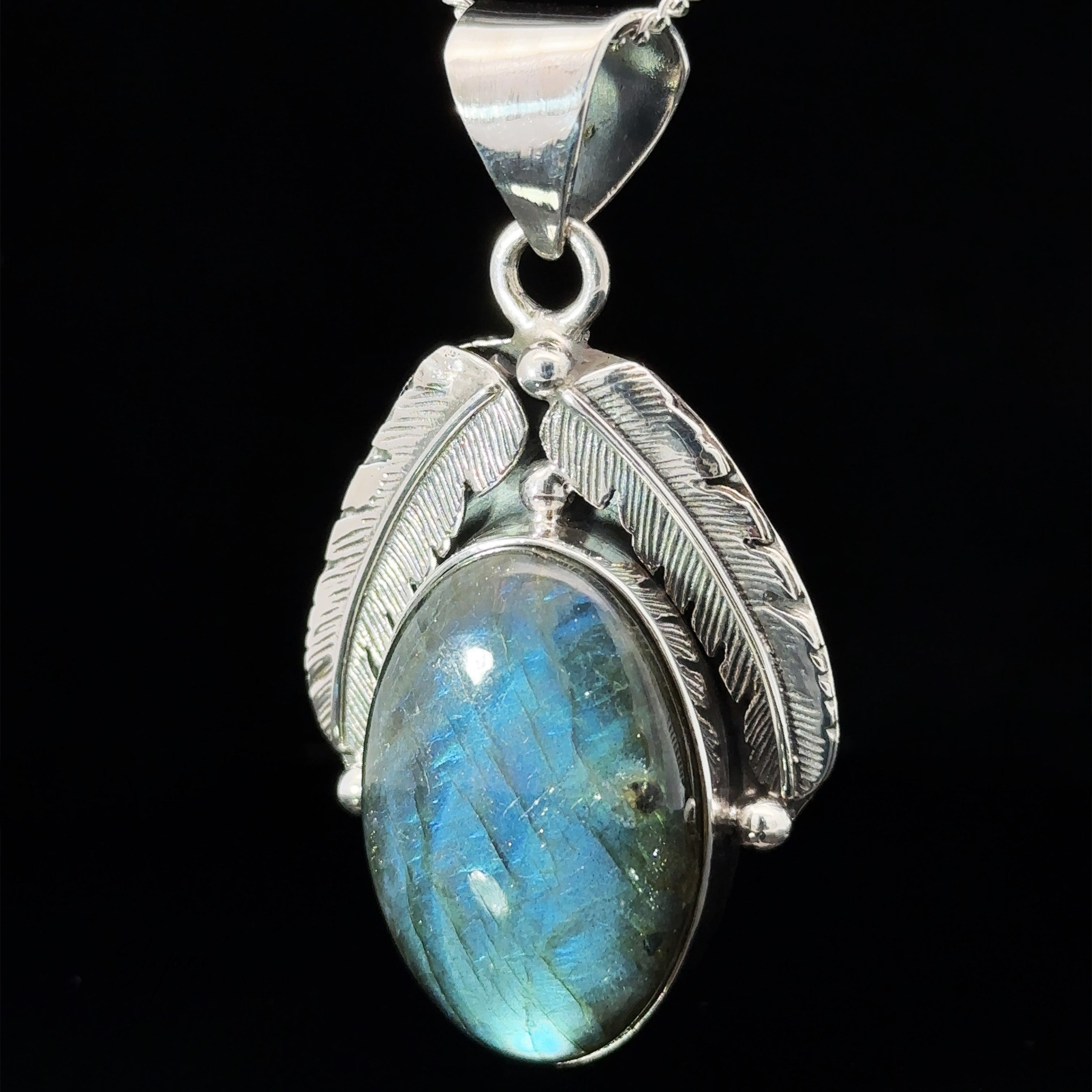 A Beautiful Southwest Stone Pendant features an oval-shaped labradorite gemstone encased by two silver feathers, perfect for those seeking a touch of western style in their jewelry collection.