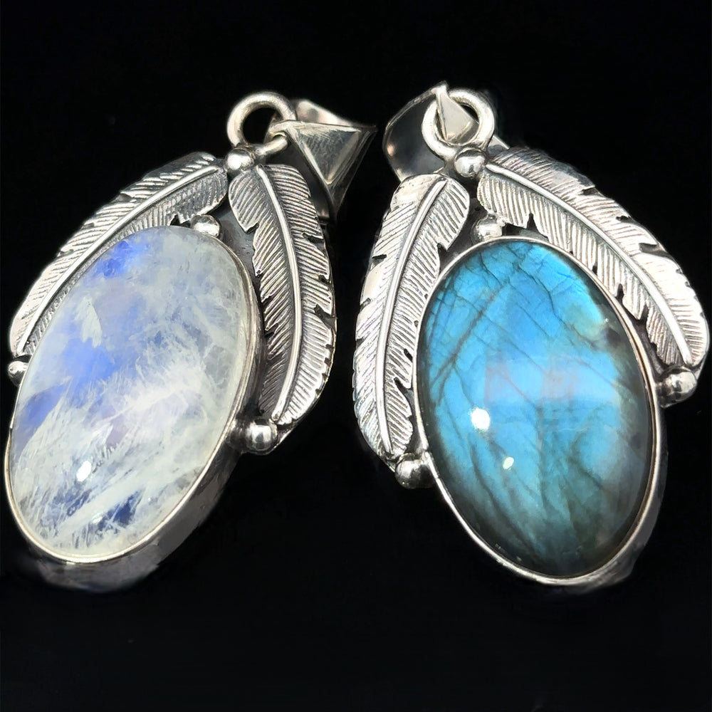Two oval Beautiful Southwest Stone Pendants, one a labradorite pendant with a blue sheen and the other resembling a moonstone pendant with a green-blue sheen, are set in sterling silver with feather detailing, against a black background.