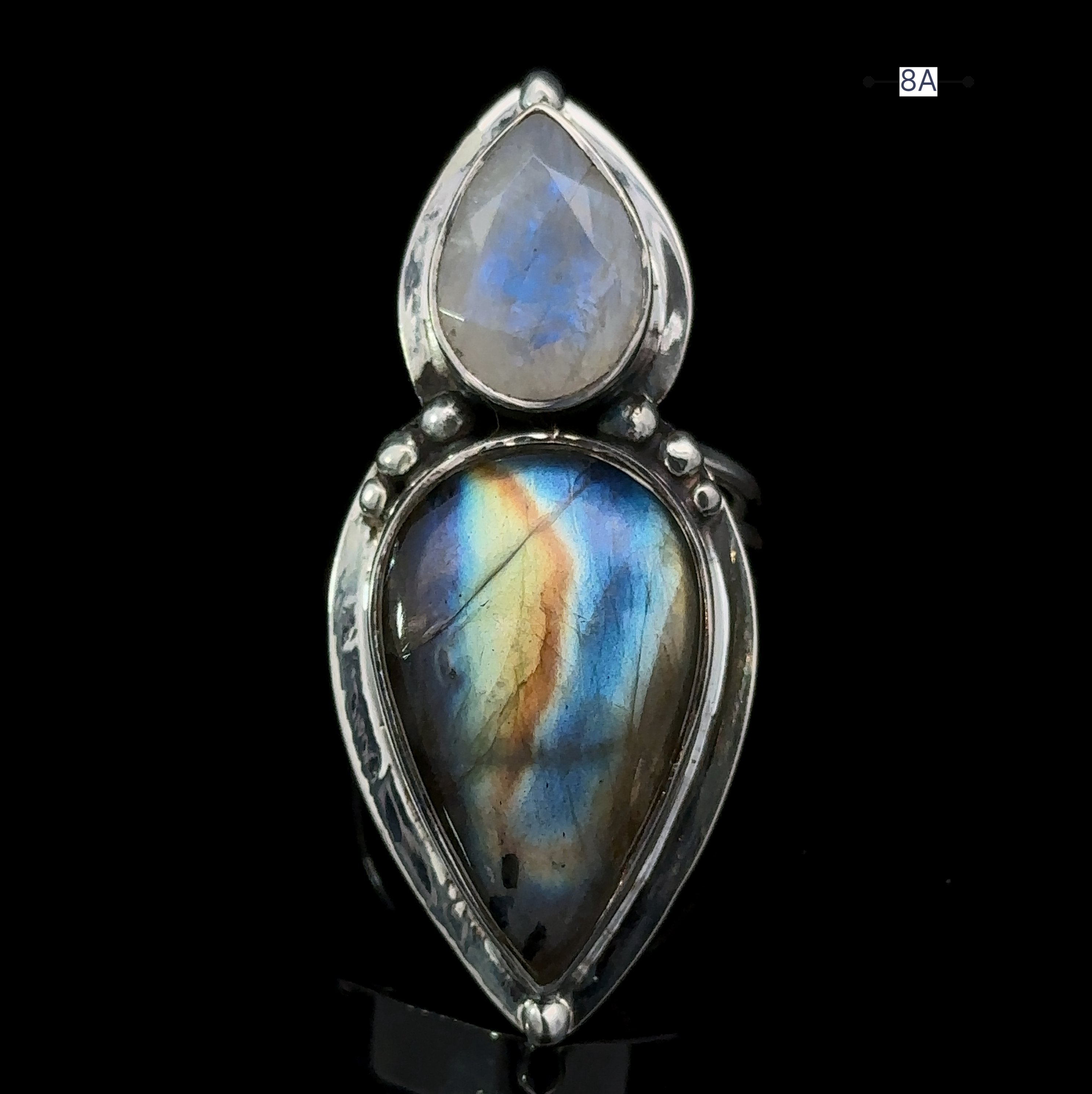 The Heavy Labradorite And Moonstone Ring is a teardrop-shaped silver statement piece featuring a polished rainbow moonstone delicately set above a larger teardrop-shaped labradorite, showcasing captivating blue, green, and yellow hues.