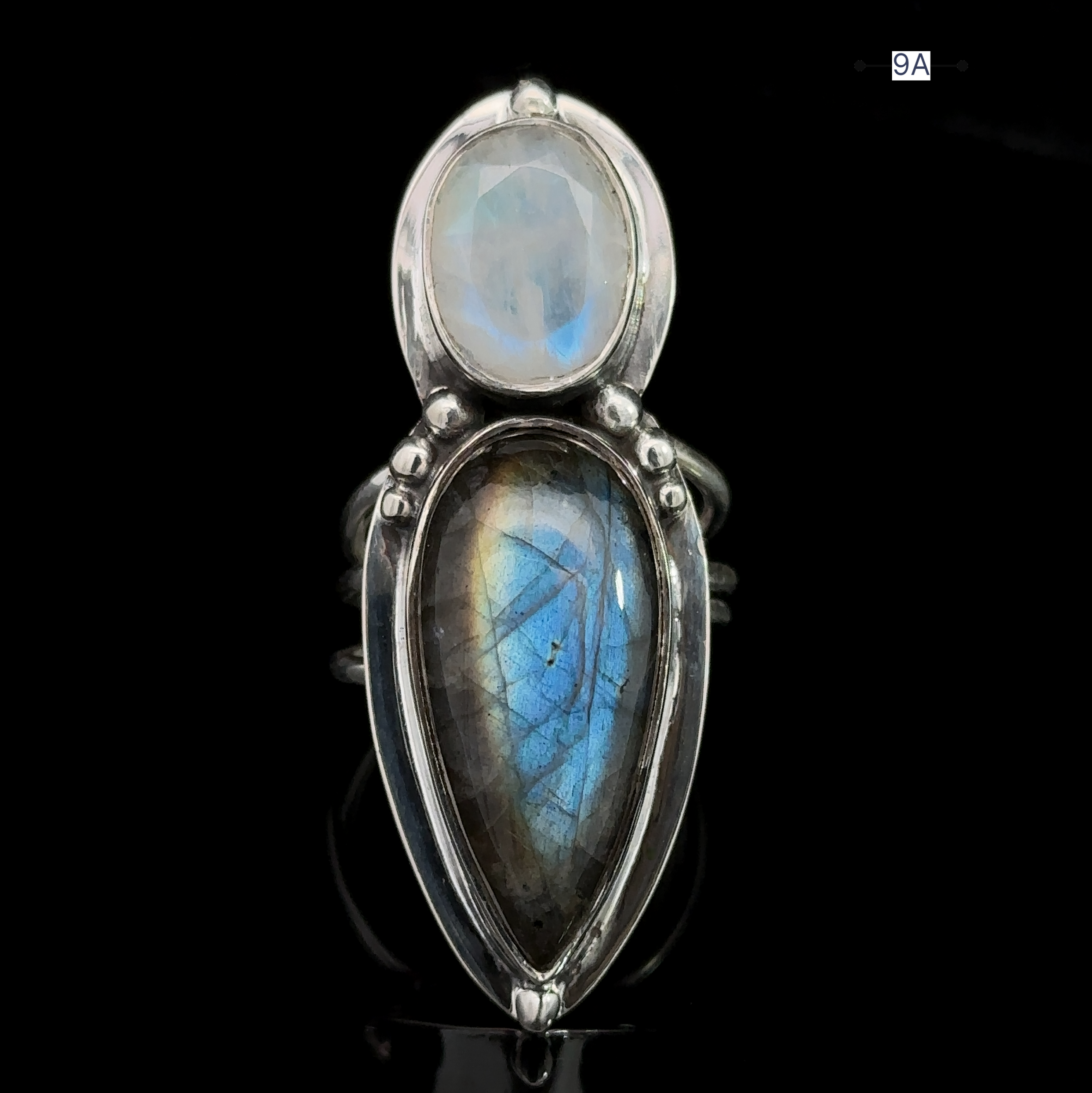 Introducing the Heavy Labradorite And Moonstone Ring, a striking piece in silver that features a captivating round moonstone on top and a teardrop-shaped labradorite below, all set against a sleek black background.