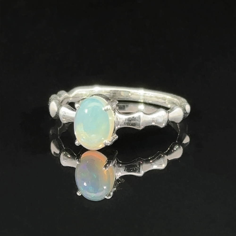 
                  
                    Pronged Oval Gemstone Ring with Textured Band with a blue topaz set on a reflective black surface.
                  
                