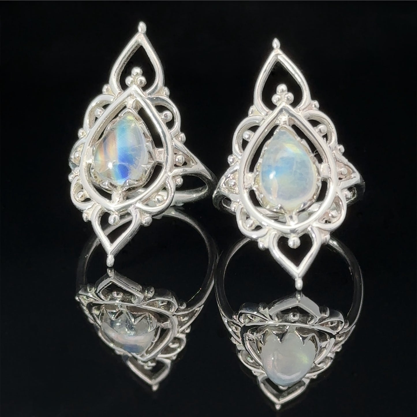 A pair of ornate silver earrings with Online Only Exclusive Designer Moonstone Ring gemstones, displayed on a reflective black surface.