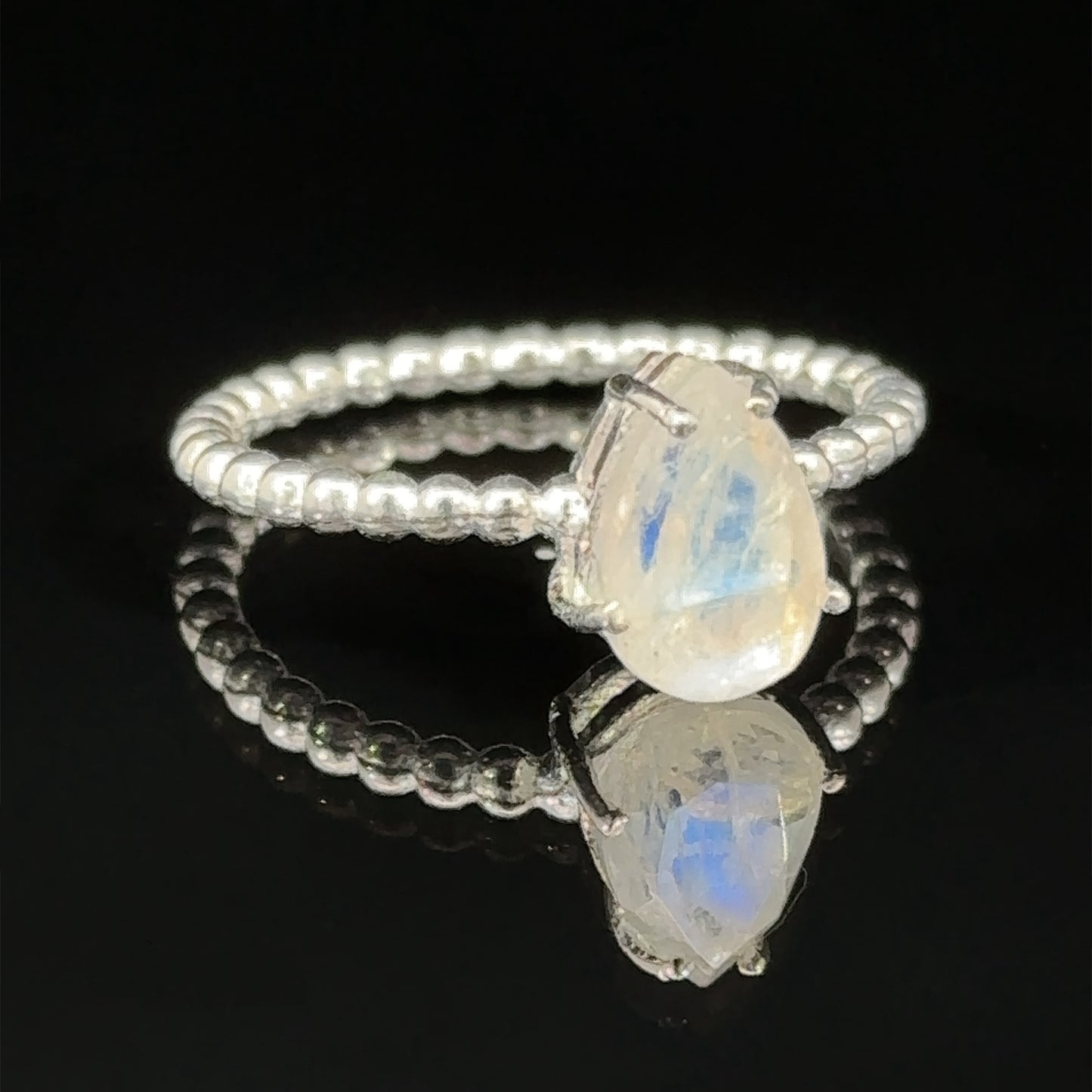 
                  
                    Vibrant Teardrop Gemstone Ring with Beaded Band with an oval opal stone, reflected on a glossy surface in a prong setting.
                  
                