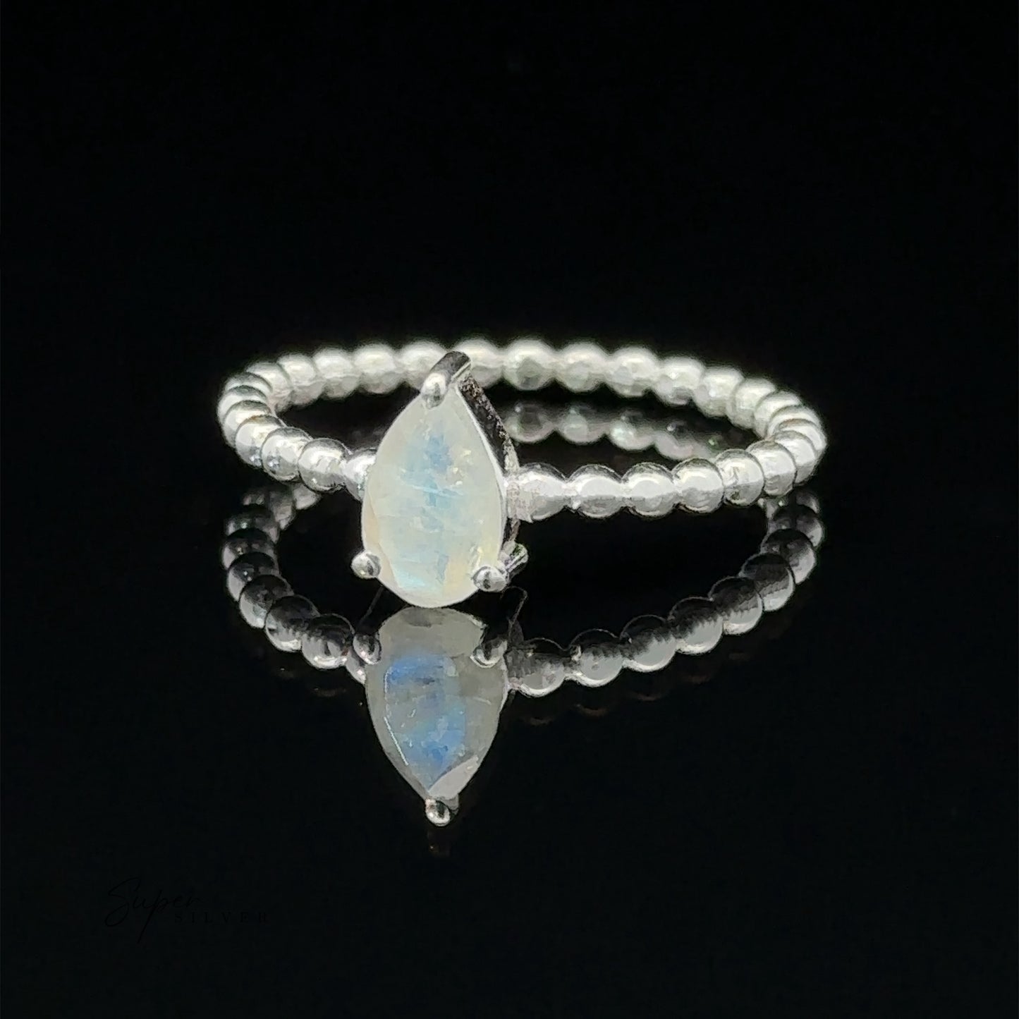 
                  
                    Sparkling Teardrop Gemstone on Beaded Band ring with two opal stones in a prong setting on a reflective surface.
                  
                