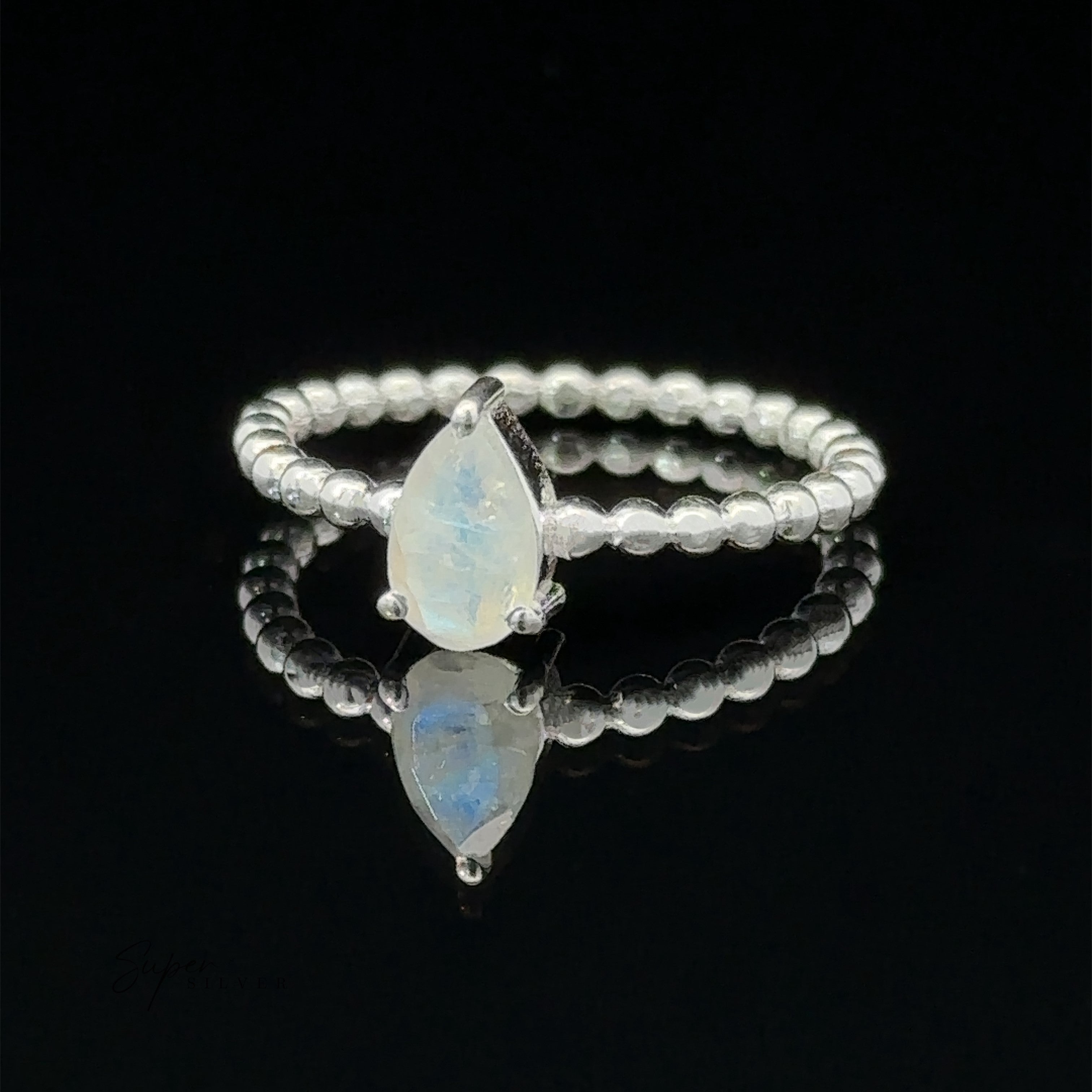 Sparkling Teardrop Gemstone on Beaded Band ring with two opal stones in a prong setting on a reflective surface.