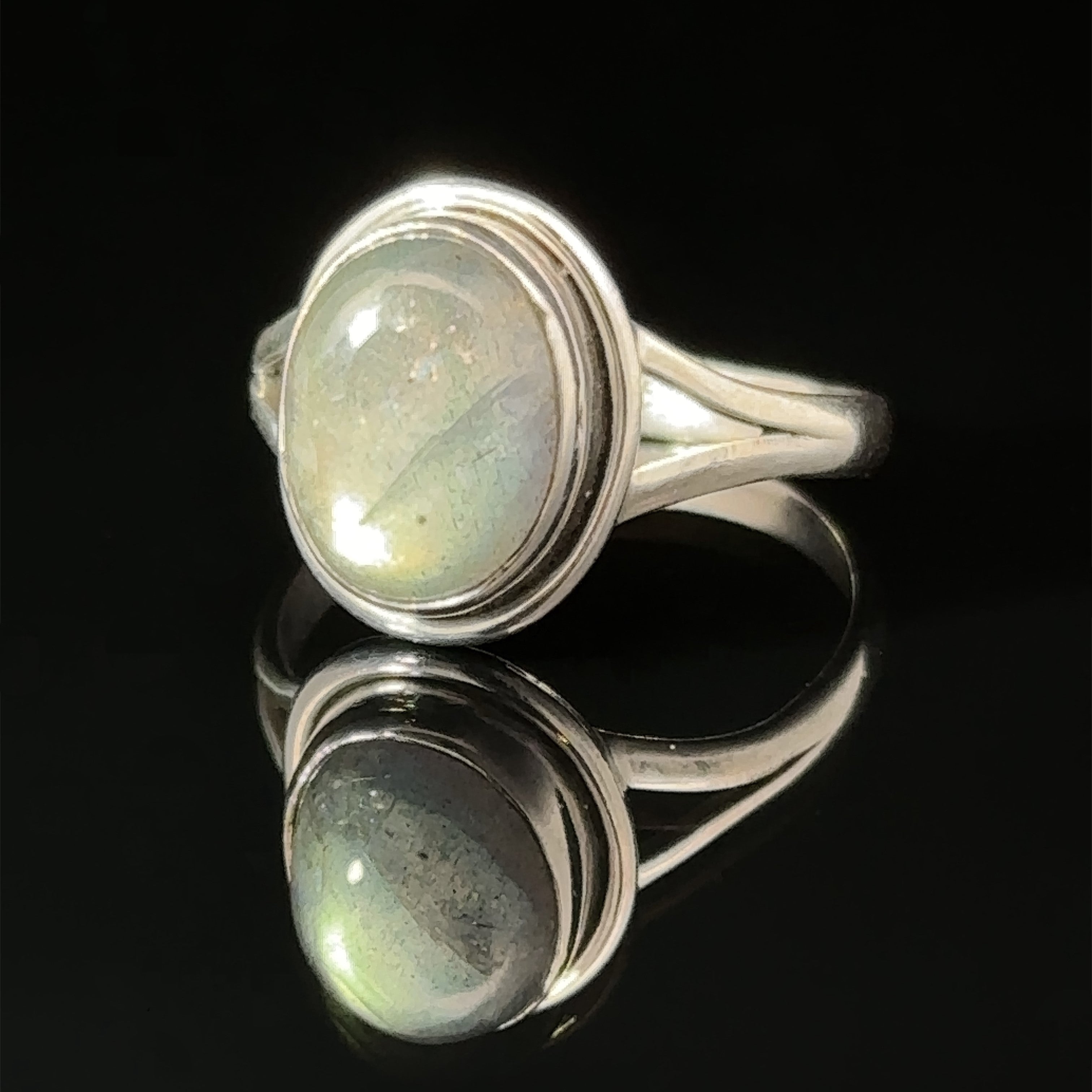 Oval split shank stone ring with an oval cabochon gemstone, reflected on a glossy surface.