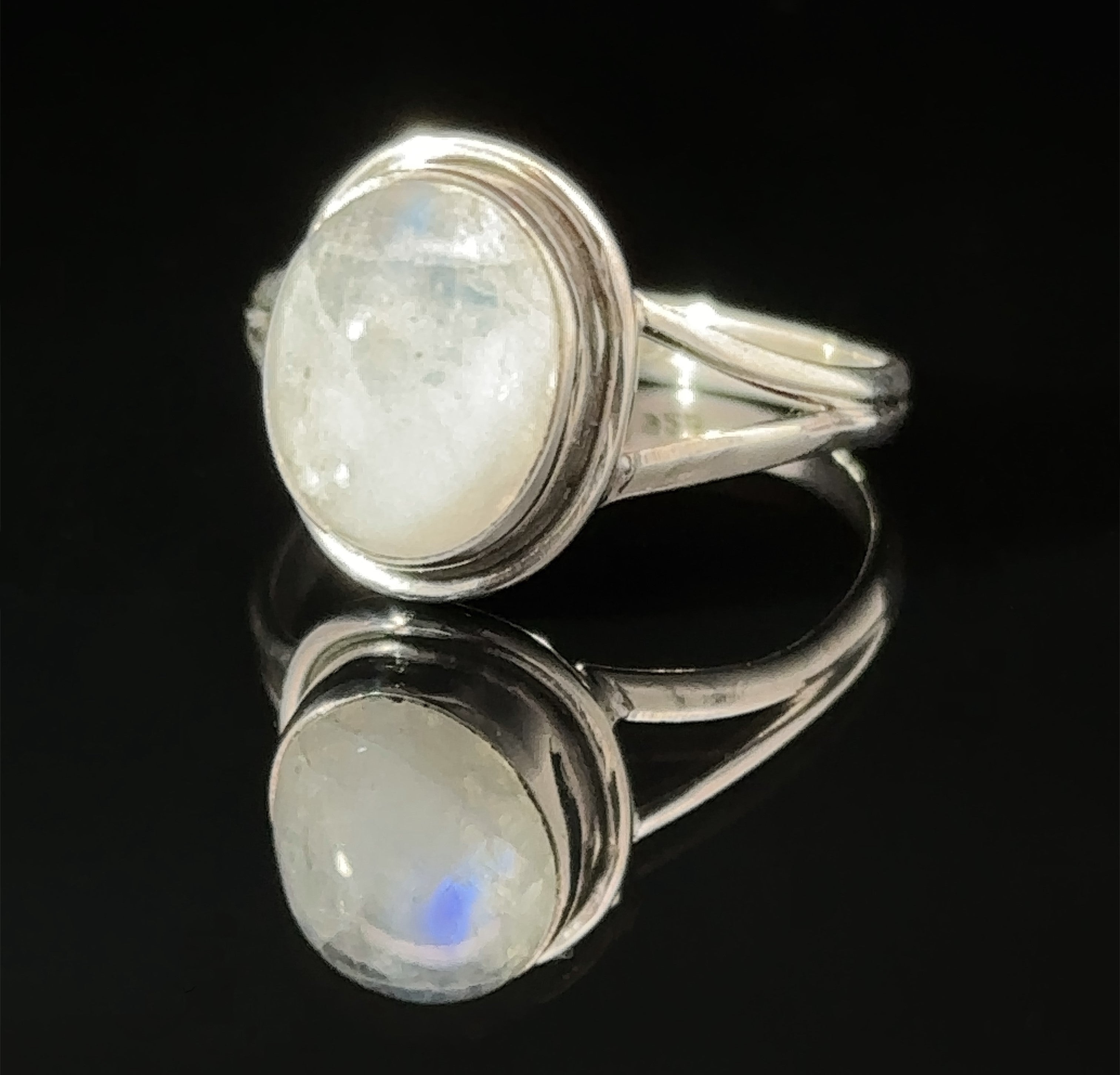 A sterling silver Oval Split Shank Stone Ring with an oval moonstone set on a reflective surface.