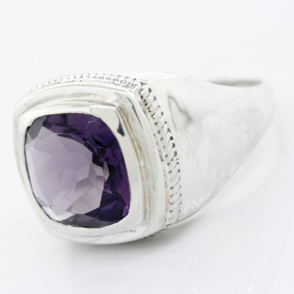 
                  
                    A Faceted Stone Signet Ring with an inset square amethyst gemstone, featuring a polished band and a textured border around the stone.
                  
                