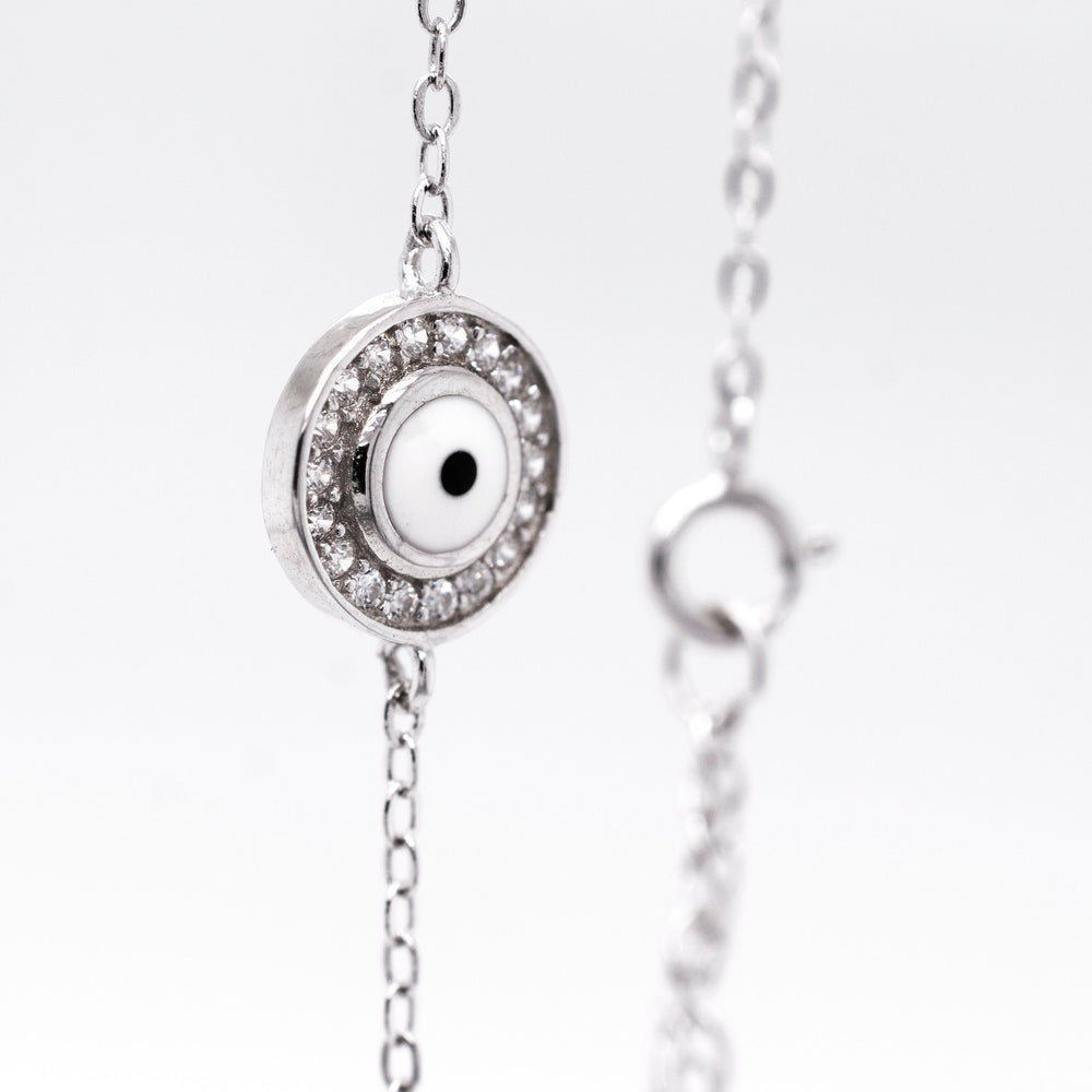 
                  
                    Close-up of a sterling silver Delicate Cubic Zirconia Evil Eye Bracelet with a round, eye-like charm surrounded by small, clear cubic zirconia gemstones. The clasp of the bracelet is visible in the background.
                  
                