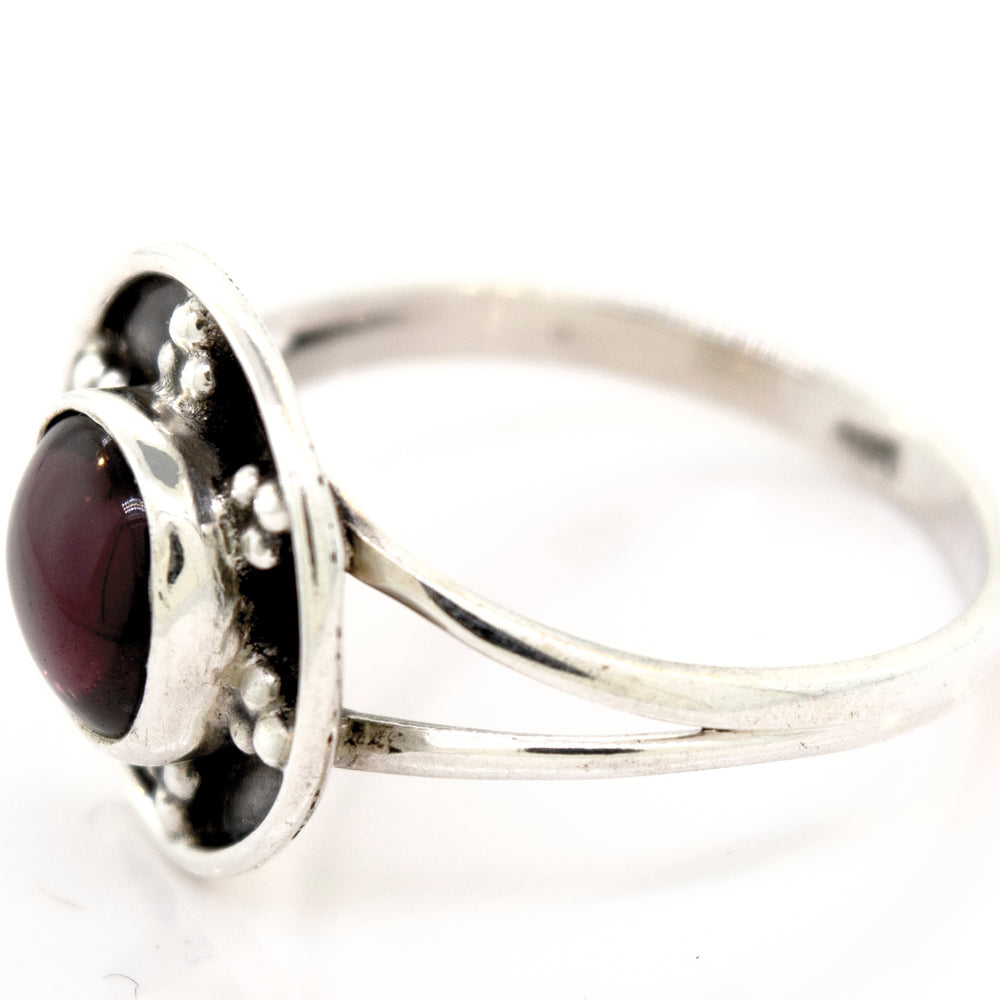 
                  
                    A Gemstone Ring With Unique Oxidized Design featuring a round, dark red stone set in a raised bezel with decorative metalwork around it. The band, made of oxidized silver, splits into two parts near the setting, showcasing intricate craftsmanship in gemstone jewelry.
                  
                