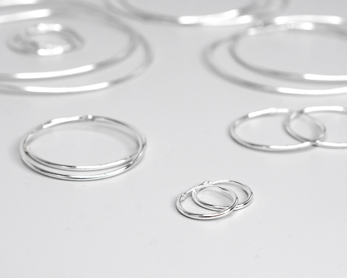 A minimalist collection of Super Silver's 1.2mm Infinity Hoops on a white surface.