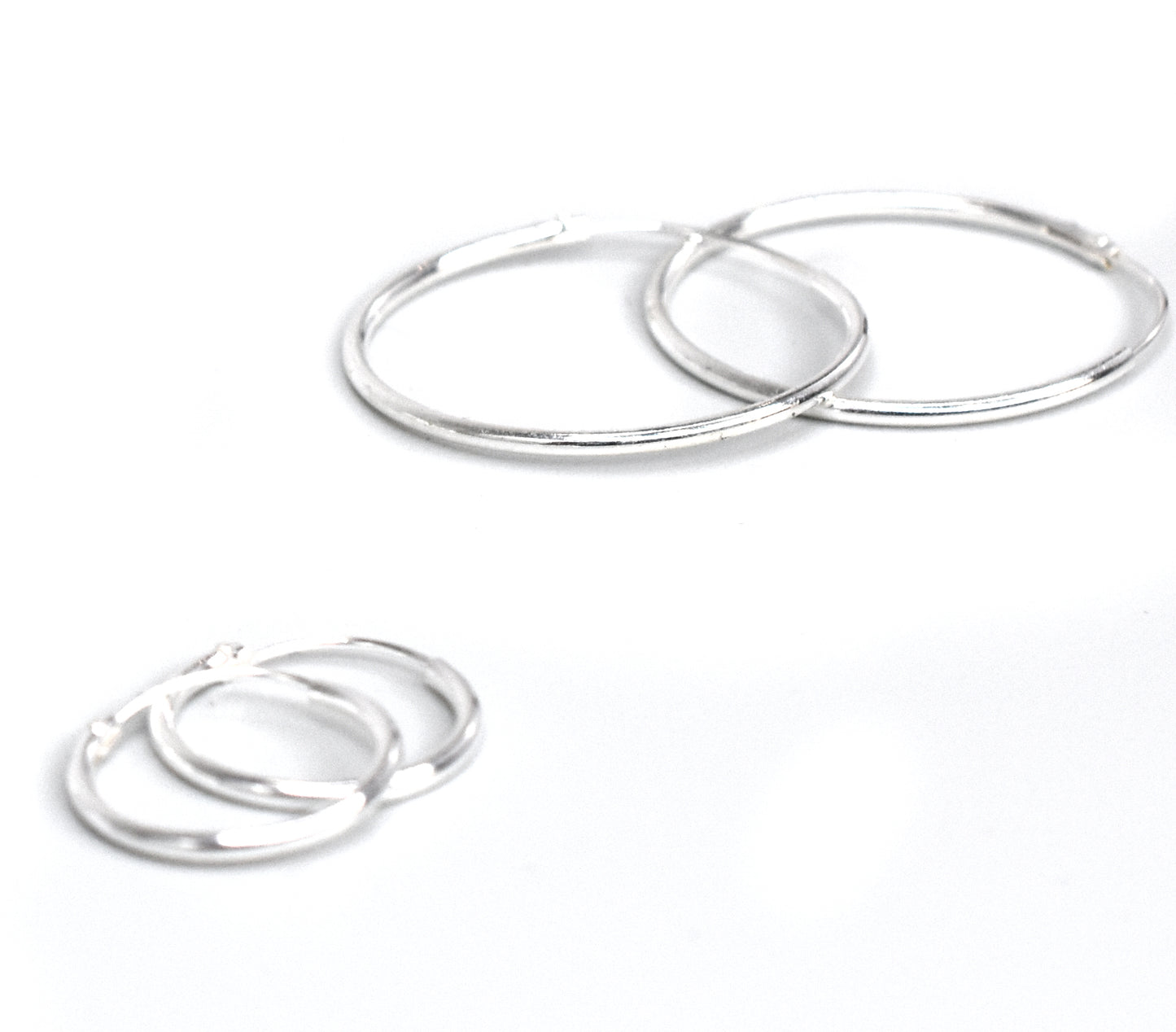 
                  
                    A pair of Super Silver 1.2mm Infinity Hoops on a white surface.
                  
                