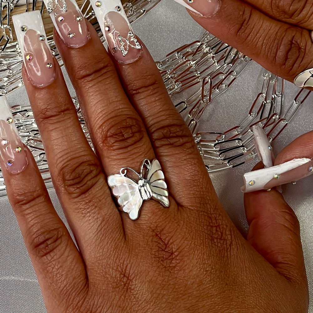 
                  
                    A woman's hand with white nails adorned with the Elegant Butterfly Inlay Ring with Swirly Antennae.
                  
                