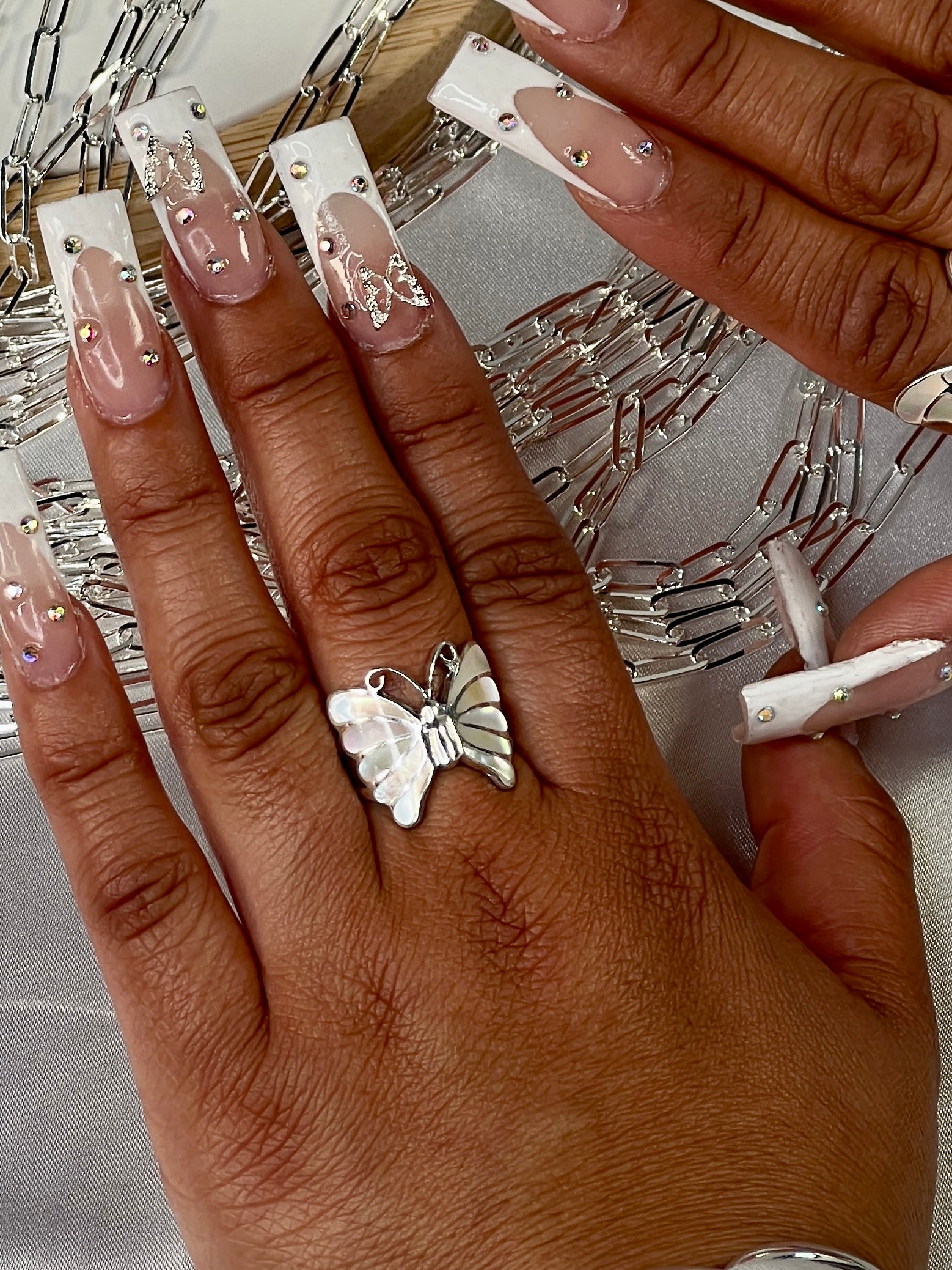 A woman's hand with white nails adorned with the Elegant Butterfly Inlay Ring with Swirly Antennae.