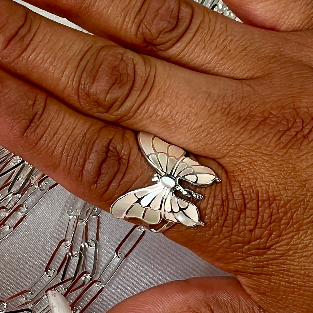 
                  
                    A woman's hand showcasing a stunning Super Silver Intricate Statement Butterfly Inlay Ring, creating a mesmerizing statement piece.
                  
                