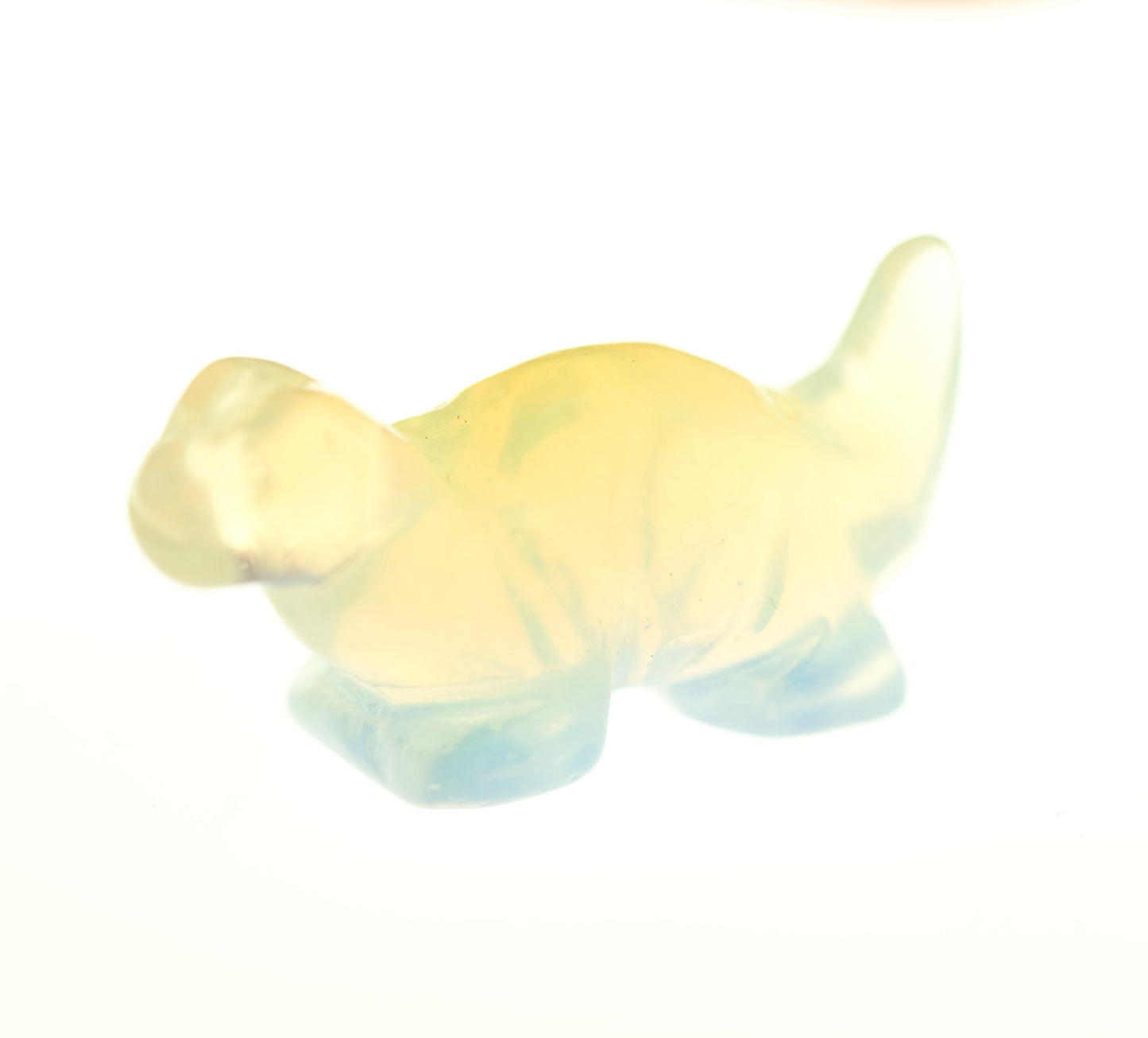 Translucent, small Carved Dinosaur Gemstone Figures in pale yellow and light blue, reminiscent of opalite, photographed against a white background.